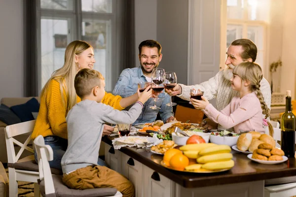 Krásná šťastná rodina cinkání sklenice vína a džusu na sváteční večeři. Rodinné cinkání sklenice při chutné večeři v útulné jídelně doma — Stock fotografie
