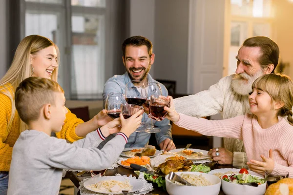 Beautiful happy family clinking glasses of wine and juice on holiday dinner. Family clinking glasses while having tasty dinner at cozy dining room at home — Stock Photo, Image