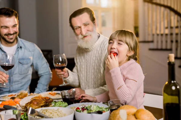 Multi Generation Family sitting at the table and having tasty dinner, celebrating Thanksgiving. Grandfather, handsome father and little daughter eating tomato and smiling — Stock Photo, Image