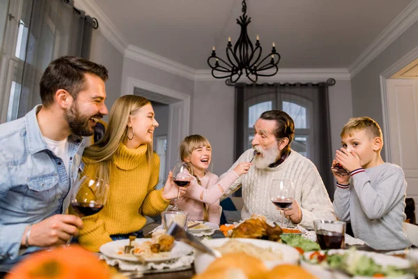 Happy family having dinner together. Little girl feeds her old grandfather and gives him tasty pasta, smiling and laughing — Stock Photo, Image