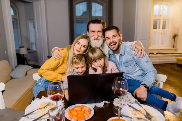 La familia alegre que celebra un Nuevo año, la Navidad o el Día de Acción de Gracias. Familia mira el portátil y sonríe. Humor festivo. Sabrosa comida en la mesa. Felices juntos . — Foto de Stock
