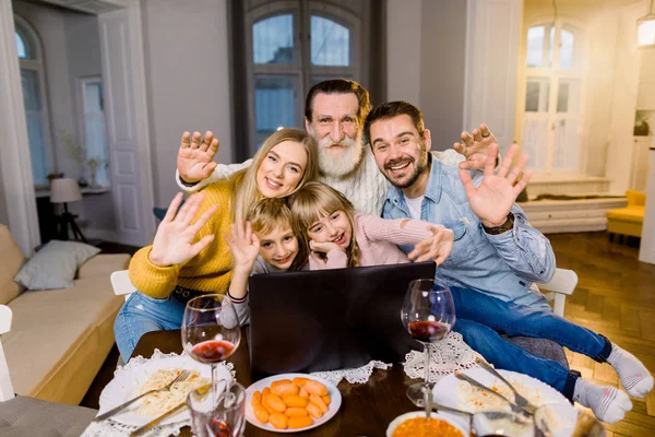 Familia feliz generación milti ver fotos o películas en un ordenador portátil mientras se sienta en la mesa festiva con la cena. Vacaciones, comida saludable y emoción positiva, concepto familiar . — Foto de Stock