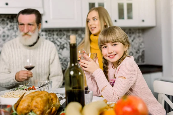 Familie, Urlaub, Generation und Menschen-Konzept - lächelnde Familie beim Abendessen zu Hause, Fokus auf kleines lächelndes Mädchen mit Glas mit Saft — Stockfoto