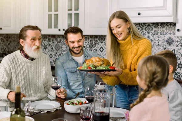 Vzrušený krásná rodina při pohledu na díkůvzdání krocana. Mladá žena drží talíř s pečeným kuřetem nebo krocanem — Stock fotografie