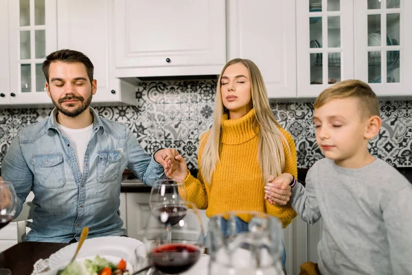 Portrait de jeune famille moderne, père, mère et fils, assis à une table festive et priant. Thanksgiving Dîner, Noël, concept vacances — Photo