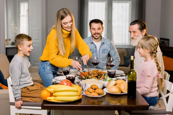 Hermosa familia feliz, abuelo, padres e hijos, celebrando juntos el día de acción de gracias. Joven bonita madre tallando pavo de Acción de Gracias — Foto de Stock