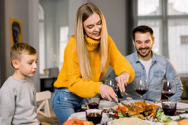 Porträt eines glücklichen Paares, das mit seinem kleinen Sohn am festlichen Tisch sitzt und gebratenen Truthahn isst. glückliche Familie beim gemeinsamen Abendessen zu Hause, während Mutter Truthahn schneidet — Stockfoto