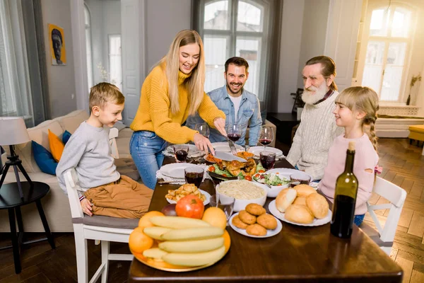 五个人的家庭，祖父、父母和孩子坐在桌旁，准备吃烤火鸡，而快乐的母亲正在切火鸡。 感恩节家庭晚餐的概念 — 图库照片