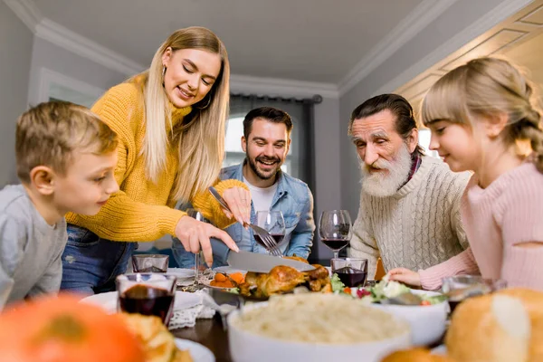 Şükran Günü yemeği yiyen iki çocuklu mutlu bir aile. Yemek masasında kızarmış hindi. Ebeveynler ve çocuklar bayram yemeği yiyorlar. Güzel anne et kesiyor.. — Stok fotoğraf