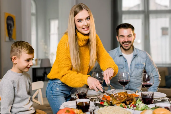 Portrait of happy couple parents and their little son sitting at festive table and going to eat roasted turkey. Happy family having delicious dinner together at home while mother cutting turkey — Stock Photo, Image