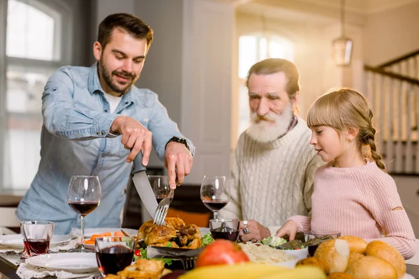 Lächelnder Vater schneidet Putenscheiben für das Familienessen. Familie mit Kindern beim Erntedankessen. gebratener Truthahn auf dem Esstisch. — Stockfoto