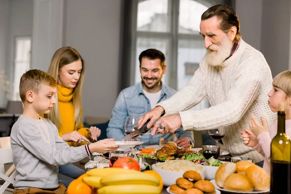 Happy grandfather cutting turkey for family on thanksgiving or christmas dinner — Stock Photo, Image