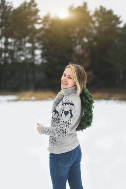 Kış ormanlarında yaşayan bir kızın elinde şık bir Noel çelengi. Kadının arka planı, kameraya bakıp gülümseyen, elinde yeni yıl çelengi tutan.