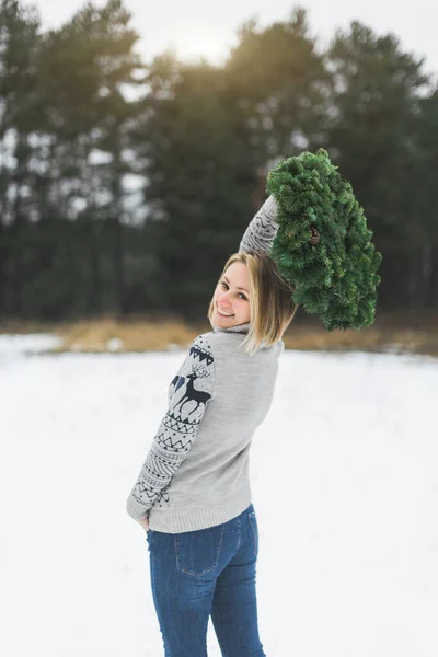 Μια όμορφη γυναίκα με πουλόβερ και τζιν κρατά ένα στεφάνι Χριστουγέννων σε εξωτερικούς χώρους, στέκεται στο φόντο του χειμώνα χιονισμένο δάσος — Φωτογραφία Αρχείου