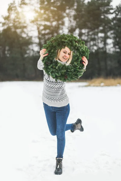 Різдво, Різдво, Різдво, Новий рік, зима, концепція щастя усміхнена жінка в сірому светрі і джинсах, позує з новорічним прикрашеним вінком, на зимовому фоні лісу — стокове фото