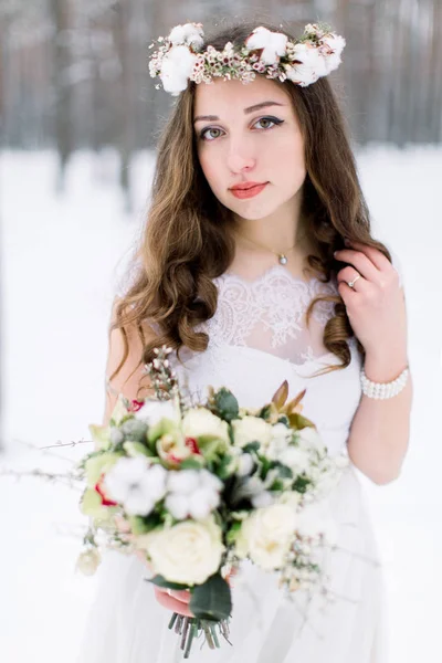 Novia con estilo en un hermoso vestido, boda en invierno, floristería para la boda, ramo y corona en la cabeza. chica con pelo largo y rizado —  Fotos de Stock