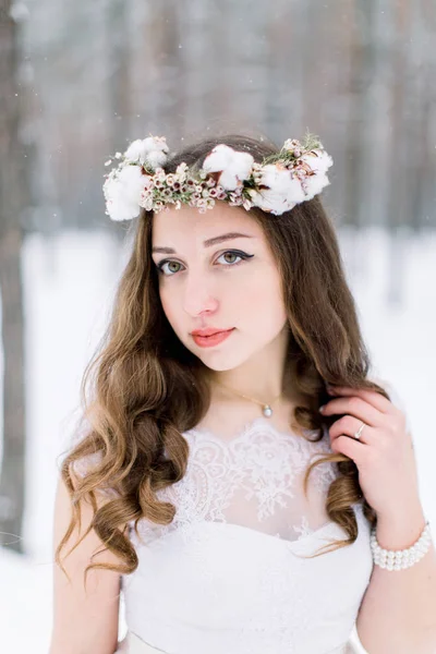 Belle mariée avec fleur et couronne de coton sur la tête, en robe de mariée sur un fond de forêt d'hiver . — Photo