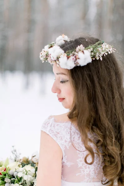 Mariage d'hiver, vue arrière de jolie mariée tenant bouquet debout dans la forêt d'hiver. Belle couronne de mariage d'hiver avec du coton et des fleurs sur la tête . — Photo