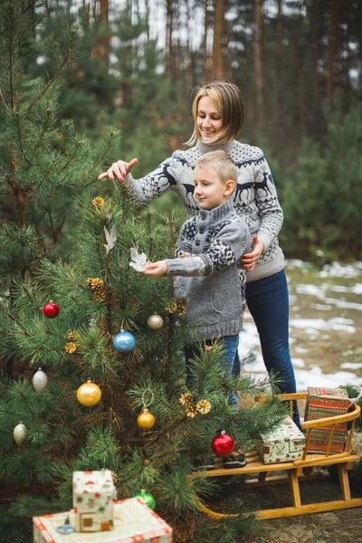 Feliz Natal e Boas Festas. Mãe e filho decorar a árvore de Natal ao ar livre. trenó de madeira e presentes, grinalda de Natal — Fotografia de Stock