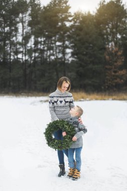Mutlu Noeller ve mutlu tatiller. Anne ve küçük oğlu kış ormanlarında birlikte yürüyorlar ve ellerinde Noel çelengi tutuyorlar. Birbirlerine bakıp gülümsüyorlar..