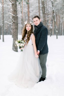 Çift, düğün, aşk konsepti. Kışın dışarıda el ele tutuşan mutlu çift. Karlı kış parkında kucaklaşan bir çift. Güzel, genç bir çiftin kışın düğünü. Gelin ve damat.