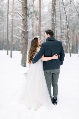 Birbirine aşık çiftlerin arka planı karlı ormanın arka planında sarılıyor. Kış düğünü.