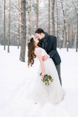 Kış düğünü. Güzel genç çift, karlı ormanda sarılıp öpüşüyorlar..