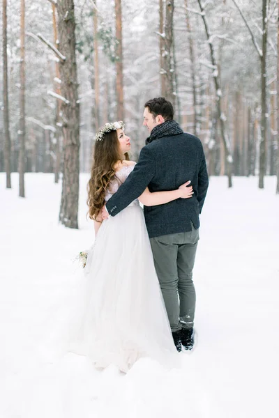 Back view of couple in love are hugging on background of the snowy forest. Winter wedding. — Stock Photo, Image