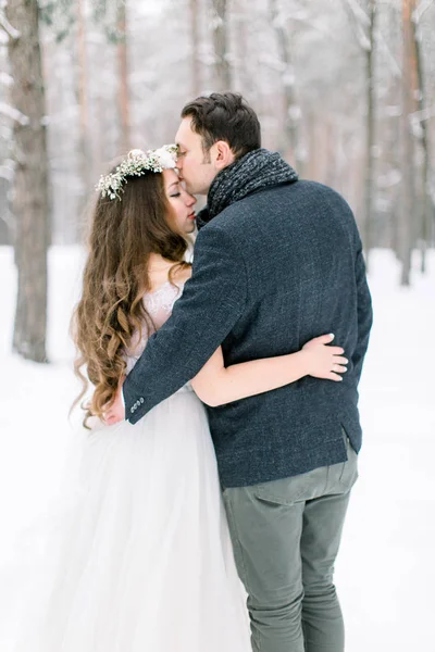 Élégant marié embrasse sa mariée sur le front sur le fond de la forêt enneigée. Mariage d'hiver — Photo