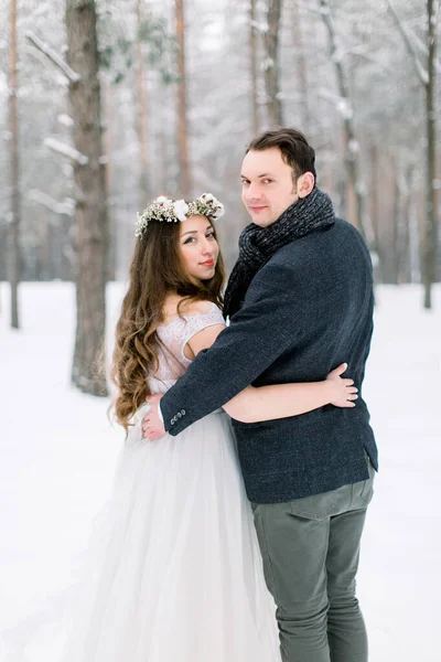 Bride in flower cotton wreath on the head and groom are hugging in the winter forest. Close-up. Winter wedding ceremony. — Stock Photo, Image