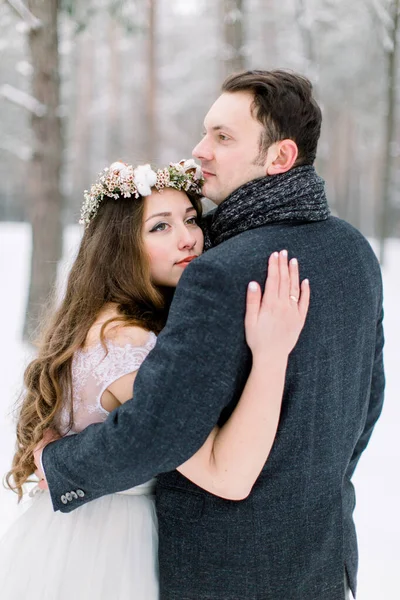 Bride in flower cotton wreath on the head and groom are hugging in the winter forest. Close-up. Winter wedding ceremony. — Stock Photo, Image
