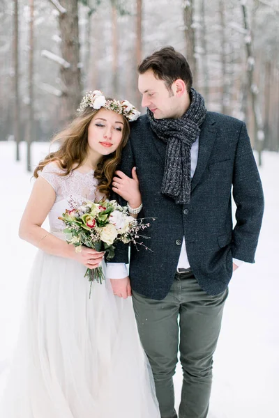 Wedding couple close-up. Bride holding the bouquet, with cotton wreath, and groom on the background of a winter landscape, forest with snow