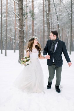 Karlı bir ormanda kış düğünü, güzel bir çift el ele tutuşuyor, birbirlerini arıyorlar, kış ormanlarında dışarıda yürüyorlar.