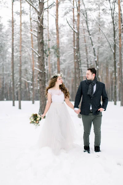 Зимняя свадьба, невеста и жених, гуляющие в снежном зимнем лесу в день свадьбы — стоковое фото