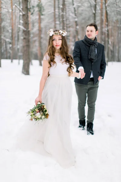 Zimní svatba. Nevěsta a ženich se drží za ruce a podívejte se na zasněžený les — Stock fotografie