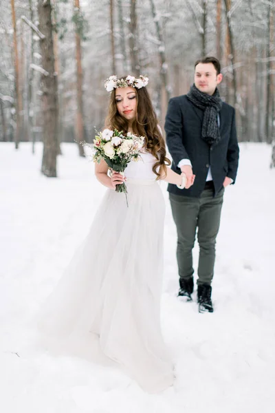 Zimní svatba. Nevěsta a ženich se drží za ruce a podívejte se na zasněžený les — Stock fotografie