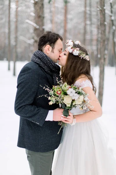 Krásná mladá nevěsta v věži na hlavě líbající svého pohledného ženicha, zimní pohádka. Zimní svatba v lese. — Stock fotografie