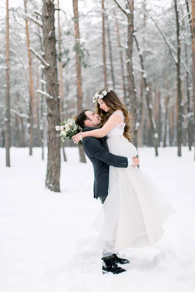 Krásná mladá nevěsta v věži na hlavě líbající svého pohledného ženicha, zimní pohádka. Zimní svatba v lese. — Stock fotografie
