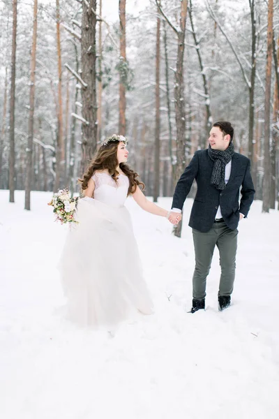 Winter wedding in a snowy forest, lovely couple holding hands, looking each other, walking outdoors in winter forest — Stock Photo, Image