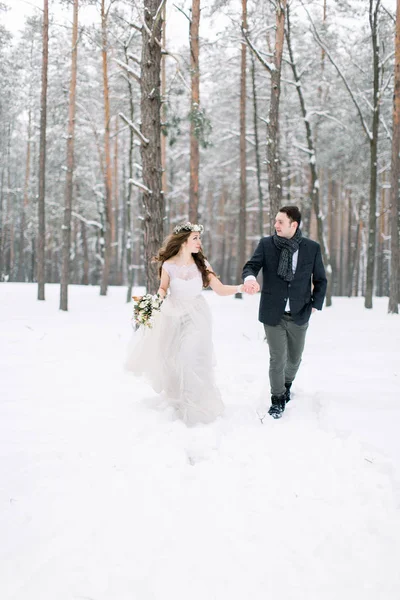 Zimní svatba ve zasněženém lese, krásný pár držící se za ruce, dívající se jeden na druhého, procházející se venku v zimním lese — Stock fotografie
