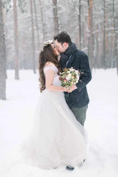 Зимняя свадебная пара, невеста и жених обнимаются и целуются в заснеженном лесу на их свадебной прогулке — стоковое фото