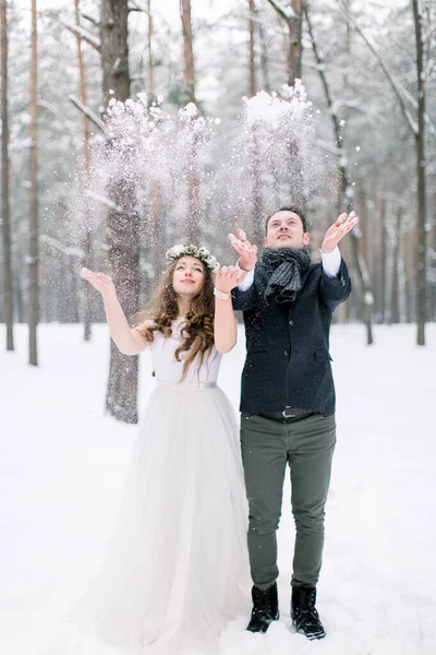 美丽的新婚夫妇站在冬天的婚礼上，站在冬天的森林里，扔着雪 — 图库照片