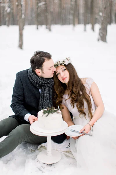 Прекрасная свадебная пара, сидящая зимой в снежном лесу. Украшенный свадебный торт — стоковое фото