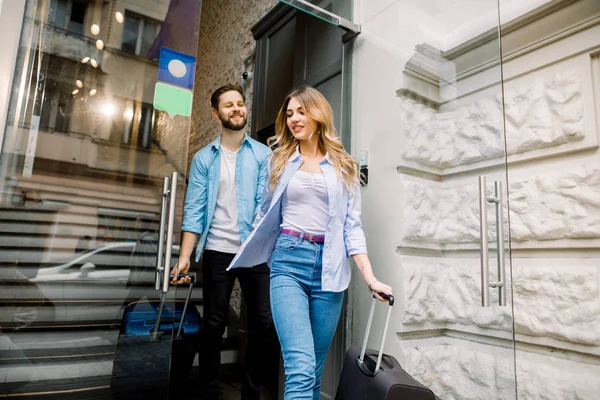 Feliz joven hombre y mujer saliendo del hotel con el equipaje —  Fotos de Stock