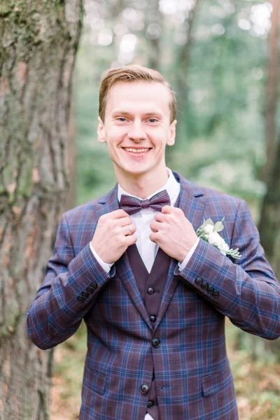 The groom portrait in forest at a wedding day. Young handsome groom in jacket posing on a wedding walk in the forest. Wedding day.
