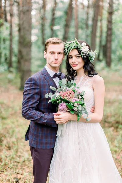 Šťastný svatební pár objímající, usmívající se a dívající se do kamery, stojící v lese. Svatební procházka venku — Stock fotografie