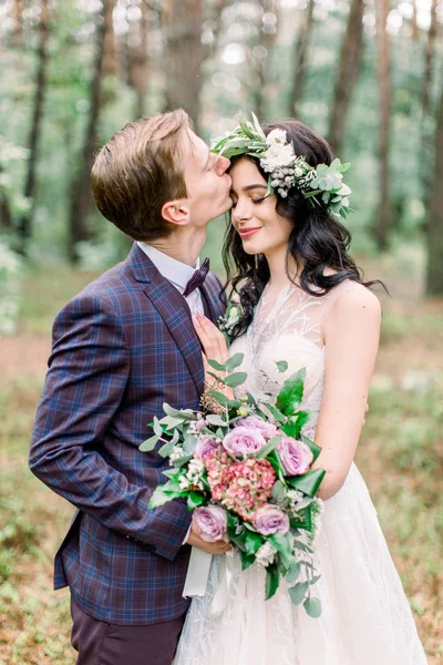 Rustik bröllop utomhus på naturen. Vacker romantisk brud och brudgum kramar, brudgummen kysser sin brud i pannan. Bröllopspromenad i skogen — Stockfoto