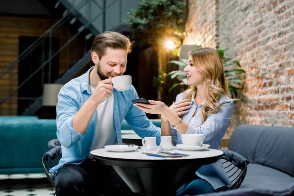 Cute young couple drinking coffee together, sitting at the table in modern loft cafe or hotel