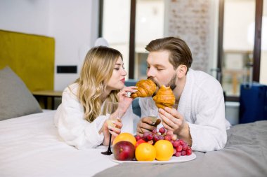 Sevgililer nişanı ya da balayını taze meyve, kruvasan ve şampanyayla kutluyor, otel odasında. Ay çöreğiyle beslenen kadın.