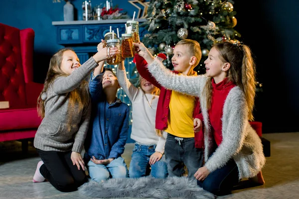 Joyeux Noël. Un groupe d'enfants sur le fond d'un sapin de Noël, buvant de la limonade et frappant des verres — Photo